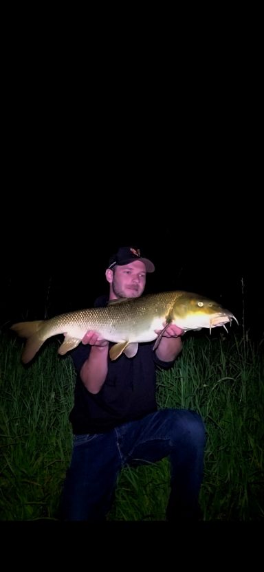 Mann kniet und hält einen großen gelben Fisch in einer dunklen Umgebung.
