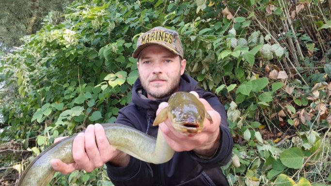 Mann hält einen großen Fisch vor einer natürlichen Hintergrundkulisse.